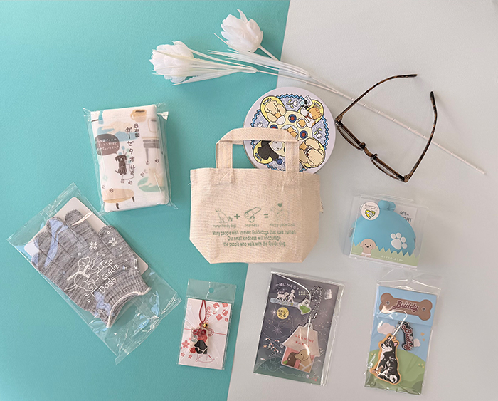 トートバッグに入るサイズの雑貨ギフトがちりばめられている。子供用手袋、クッキー、キーホルダー、ポチのポチ、フェイスタオル、見守りなど